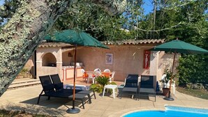 Zona de piscina con sillones de descanso y sombrillas, una pequeña mesa y un muro de azulejos.