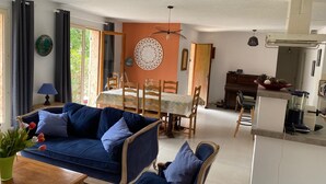 Una sala de estar con un sofá azul, una mesa de comedor con sillas, una zona de cocina con una licuadora y vistas a zonas verdes.