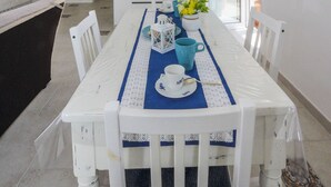 A dining area with a white table, blue placemat, and white chairs. There is a kitchen in the background with white cabinets and a microwave. - Villa Salice with private hot tub and solarium (Amalfi)