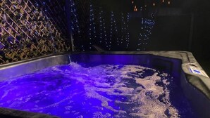 A hot tub with a blue light feature, surrounded by a decorative wall with a lattice design and string lights.