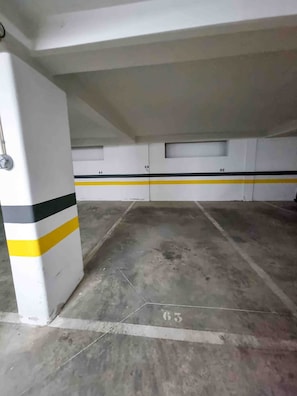 An underground parking garage with white walls, yellow and black stripes, and concrete floors marked with numbers. - Flat Praia Rocha Tower Sunset (Portimão)
