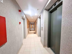 A modern hallway with a tiled floor, a red emergency exit sign, and an elevator on the right. - Flat Praia Rocha Tower Sunset (Portimão)