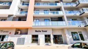 A modern high-rise building with multiple balconies and a ground-level entrance labeled "Rocha Tower."