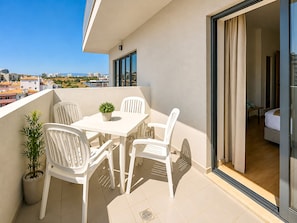 A balcony with white chairs, a table, and a potted plant. - Flat Praia Rocha Tower Sunset (Portimão)