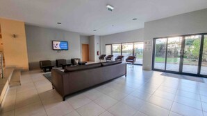 A modern lobby with a sofa, chairs, a TV, and a glass door leading outside.