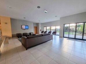 A modern lobby with a sofa, chairs, a TV, and a glass door leading outside.