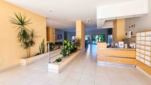 A modern reception area with a wooden desk, a plant display, and a tiled floor.