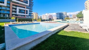 Una piscina con sillones de descanso, rodeada de modernos edificios de apartamentos.