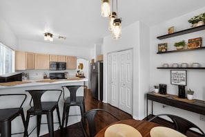 A modern kitchen with wooden cabinets, a central island, bar stools, and a dining table.