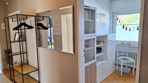 Una habitación con armario espejado, radiador blanco, ventana con vistas y una silla blanca.