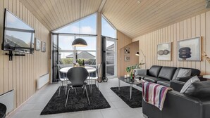 Un salon moderne avec un canapé en cuir noir, une table à manger avec des chaises et une grande fenêtre laissant entrer la lumière naturelle.