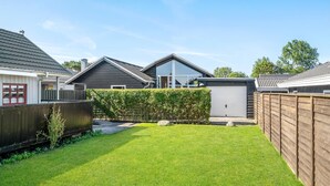 Un jardin arrière d’une maison, avec une pelouse bien entretenue, une clôture en bois et un garage.