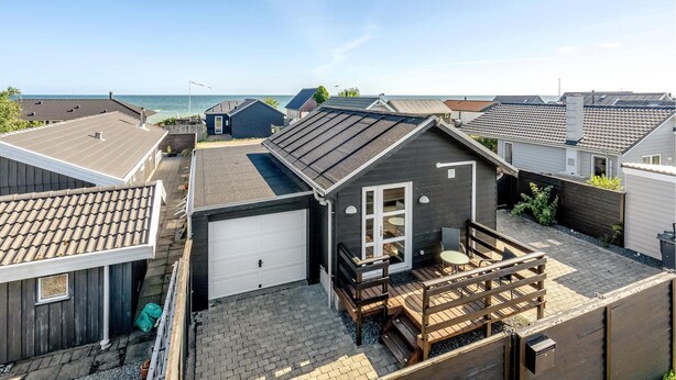 Un quartier résidentiel avec une maison dotée d’un garage, d’une petite terrasse avec mobilier d’extérieur et d’une vue sur la mer.