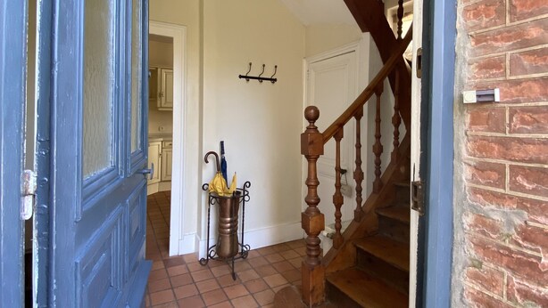 A hallway with a blue door, a tiled floor, a wooden staircase, and a wall-mounted light fixture.