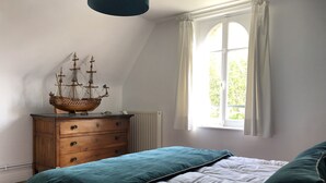 A bedroom with a wooden dresser, a bed with teal and white bedding, and a window with curtains.