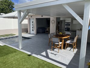 Ein überdachter Außenbereich mit Essbereich, Pool, Küche und Wohnzimmer.