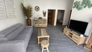 Un salon moderne avec un canapé gris, une table basse en bois, un meuble pour la télévision et un grand téléviseur.