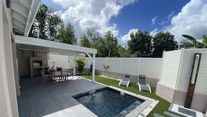 Un espace piscine extérieur moderne doté d’une terrasse, de coins salon et d’une partie abritée.
