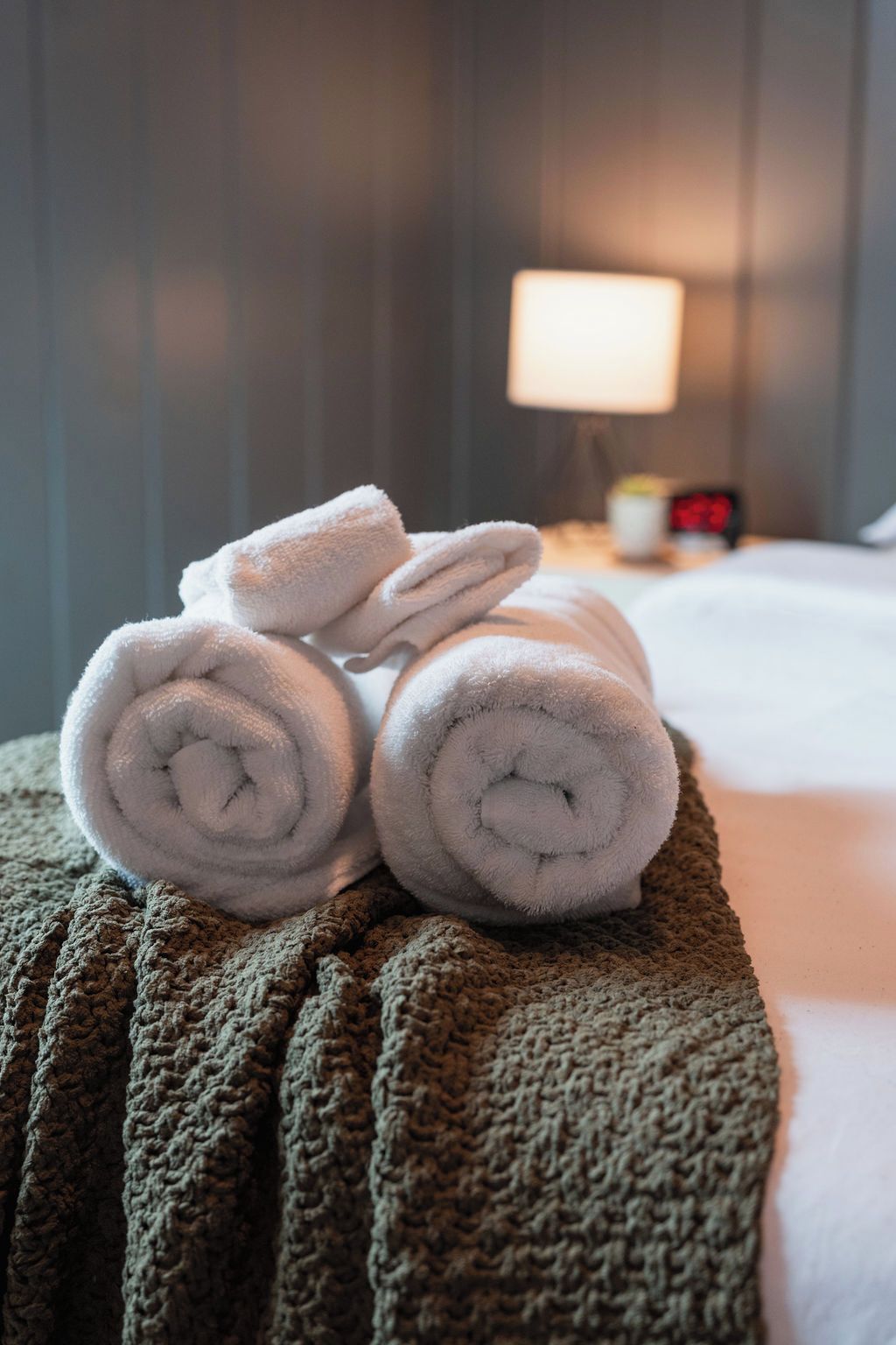 A stack of rolled towels on a textured green ottoman in a hotel room.
