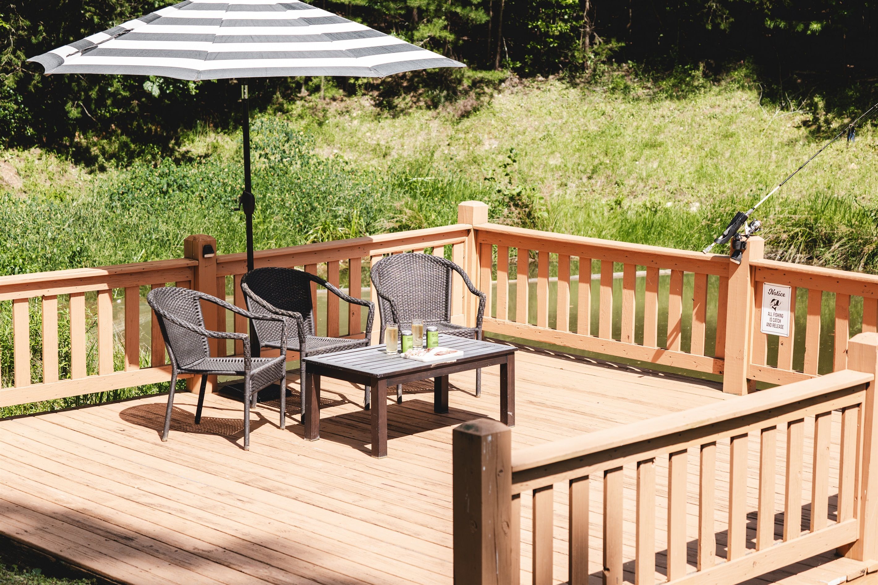 Une terrasse en bois avec deux fauteuils en osier et une table, un parasol et une canne à pêche.