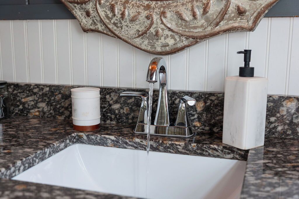 A bathroom with a granite countertop, a white sink, a faucet, a soap dispenser, and a cup.