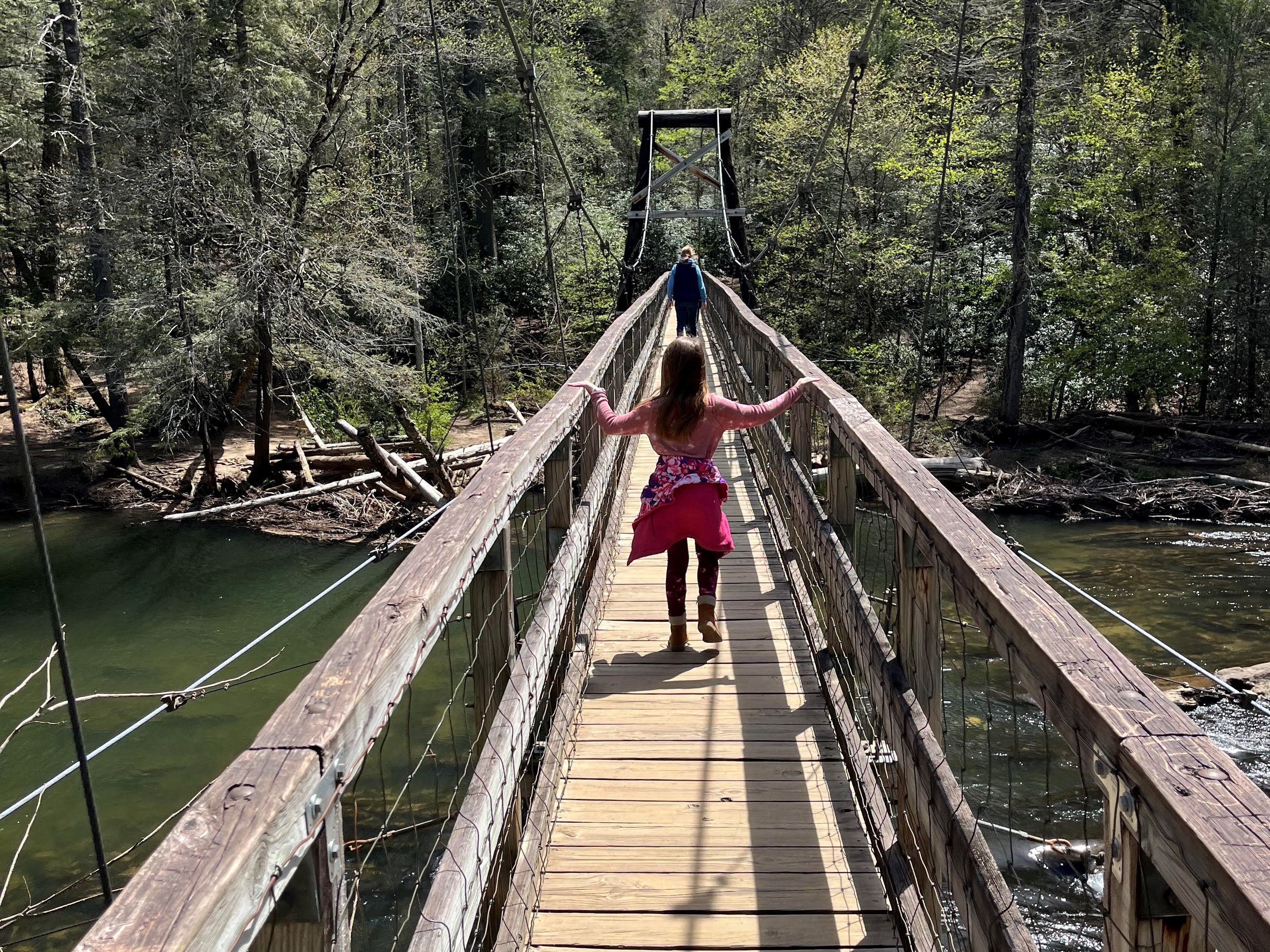 A wooden suspension bridge over a river surrounded by trees.