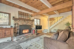 Una sala de estar acogedora con chimenea de ladrillo, vigas de madera, una escalera y un sofá cómodo.