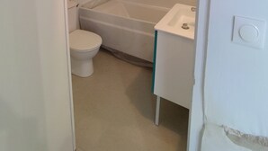 A small, white bathroom with a toilet, a bathtub, and a sink. - Fully Equipped Furnished Design (Poissy)