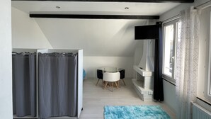 A compact, modern room with a shower, a small table, and a window with patterned curtains. - Fully Equipped Furnished Design (Poissy)
