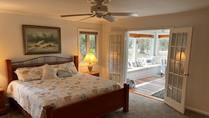 A bedroom with a wooden bed, a ceiling fan, a window with blinds, and a view of a patio area.