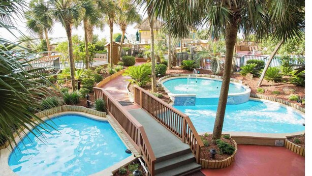 Un área de piscina con dos jacuzzis, rodeada de palmeras y una terraza de madera.