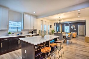 A modern kitchen with dark cabinets, a white island, and bar stools. - 4 Mi to Dtwn Dallas: Home w/ Fire Pit + Gazebo (Dallas)