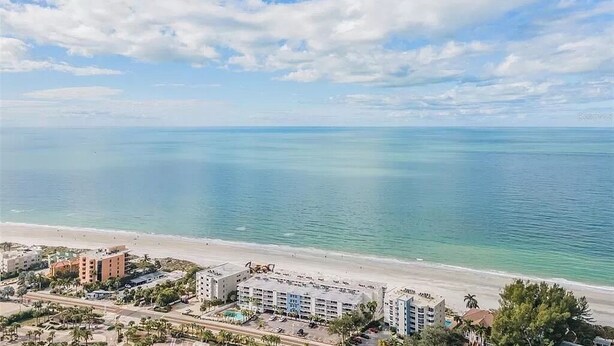 A coastal hotel with multiple buildings, a beach, and a clear sky.