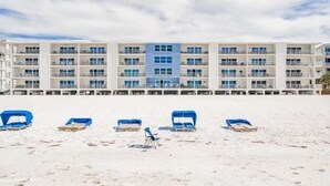 A beachfront hotel with multiple balconies, a sandy beach in the foreground, and a clear sky.