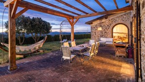 A covered outdoor patio with a stone wall, a hammock, and outdoor furniture. - Ribusieri Country House (Cinigiano)