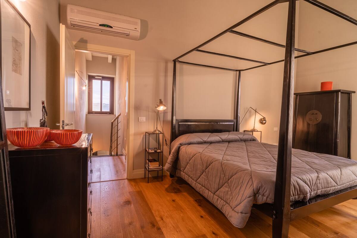 Una cama con dosel, un cabecero, una mesita de noche con lámpara y un armario.
