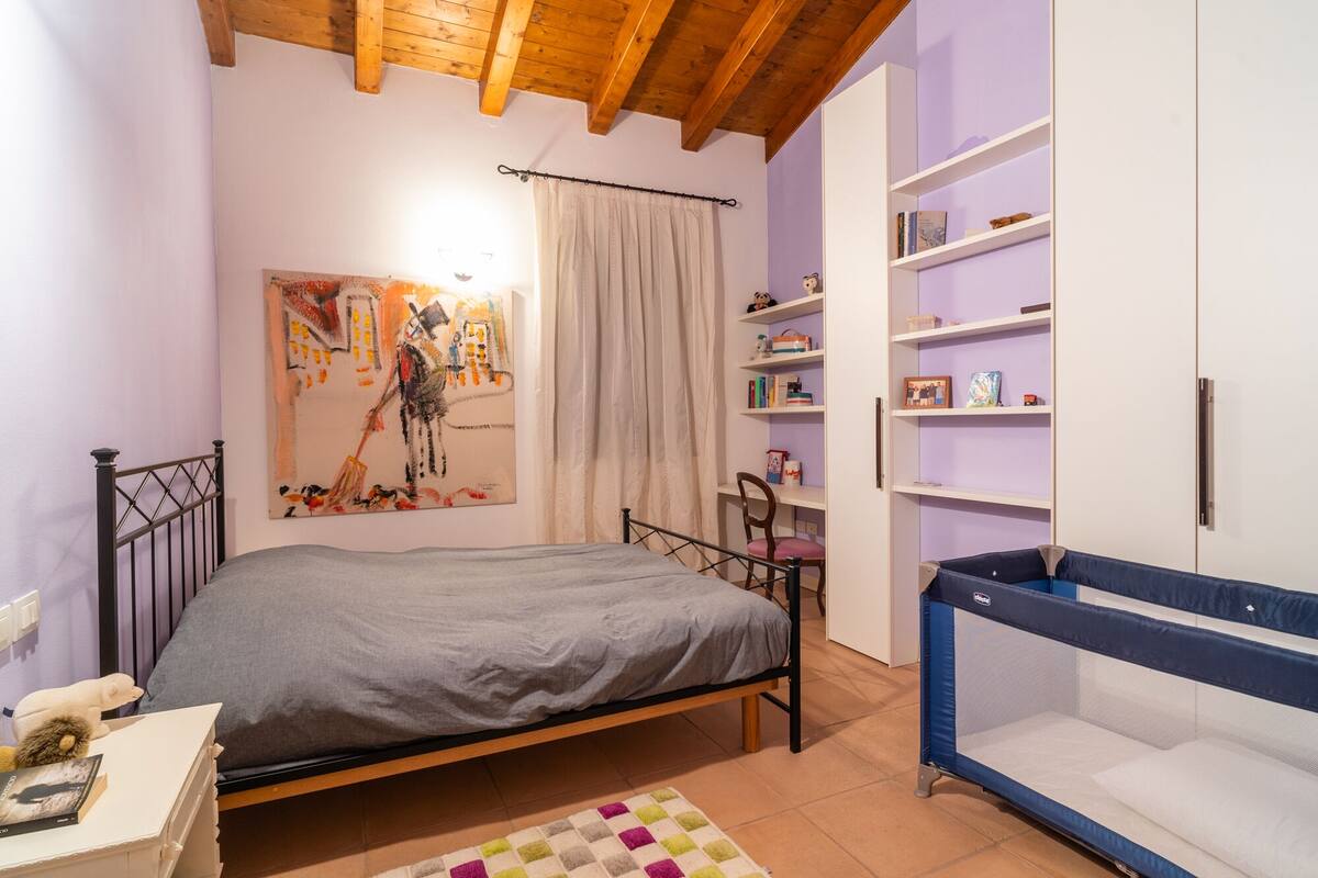 Un dormitorio con cama, cuna, estantería y un cuadro en la pared.