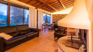 A modern living room with a leather sofa, a dining table with chairs, and a stone fireplace. - Ribusieri Country House (Cinigiano)