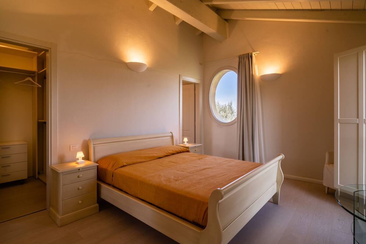 Un dormitorio con cama, mesitas de noche, armario y ventana con cortinas.