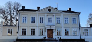 A large, two-story building with a symmetrical facade, multiple windows, and a central entrance with a wooden door.
