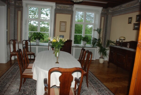 A dining room with a large table, chairs, and potted plants.