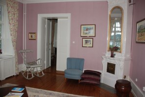 A room with wooden flooring, a rocking chair, a blue armchair, a fireplace, and framed pictures on the wall.