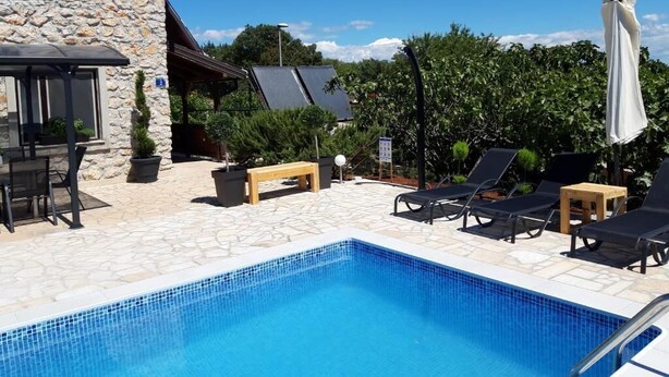 Ein Poolbereich mit Liegestühlen, ein Steinhaus und eine überdachte Sitzgruppe.