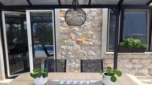 Eine Terrasse im Freien mit einer Steinmauer, einem Tisch mit Stühlen, Blumentöpfen und einer hängenden Leuchte.
