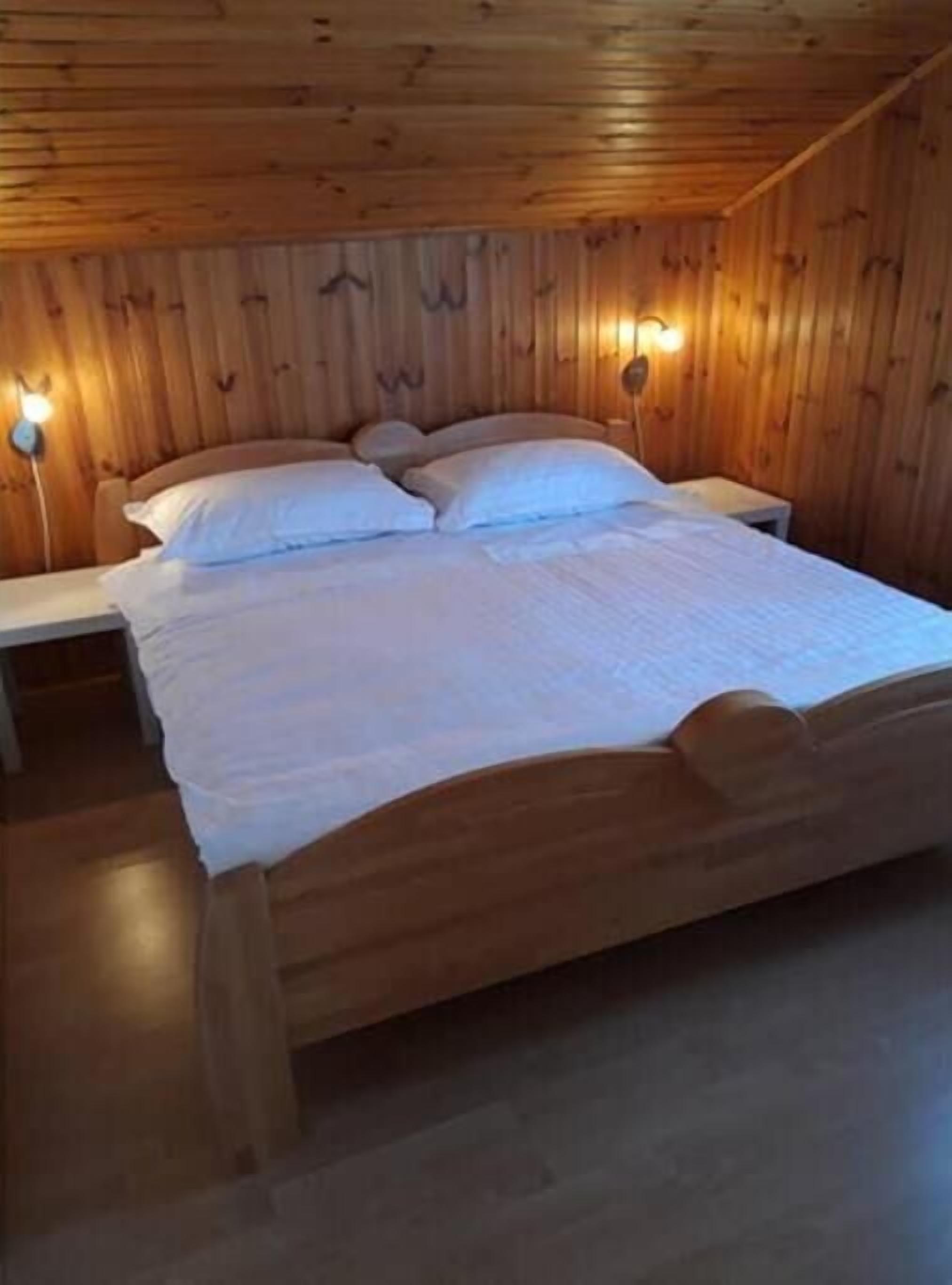 A wooden-paneled bedroom with a bed, two bedside tables, and wall-mounted lamps.