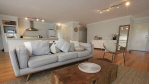 Ein modernes Wohnzimmer mit einer Couch, einem Couchtisch und einer dahinterliegenden Küchenzeile.
