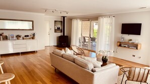 Ein modernes Wohnzimmer mit einer Couch, einem Essbereich mit einem weißen Schrank, einem an der Wand befestigten Fernseher und einer Glastür zum Außenbereich.