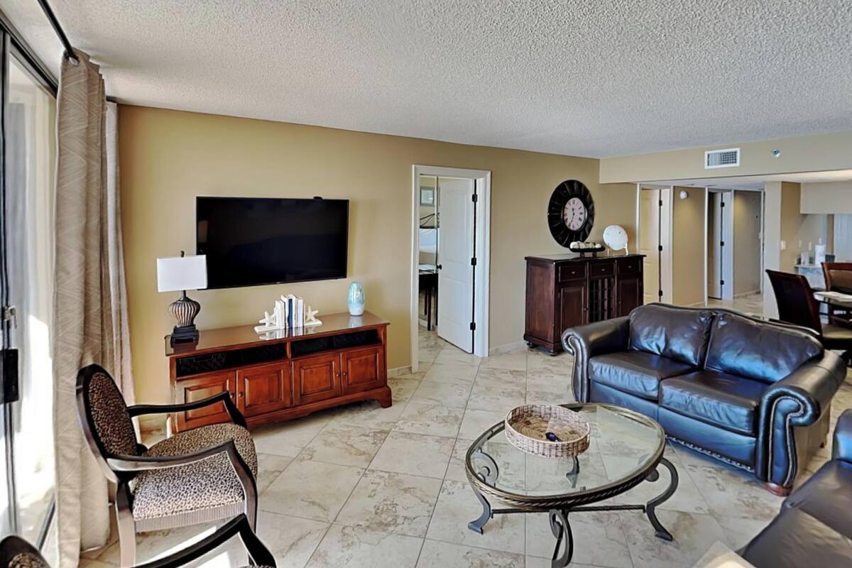A living room with a TV, leather sofa, and a glass coffee table.