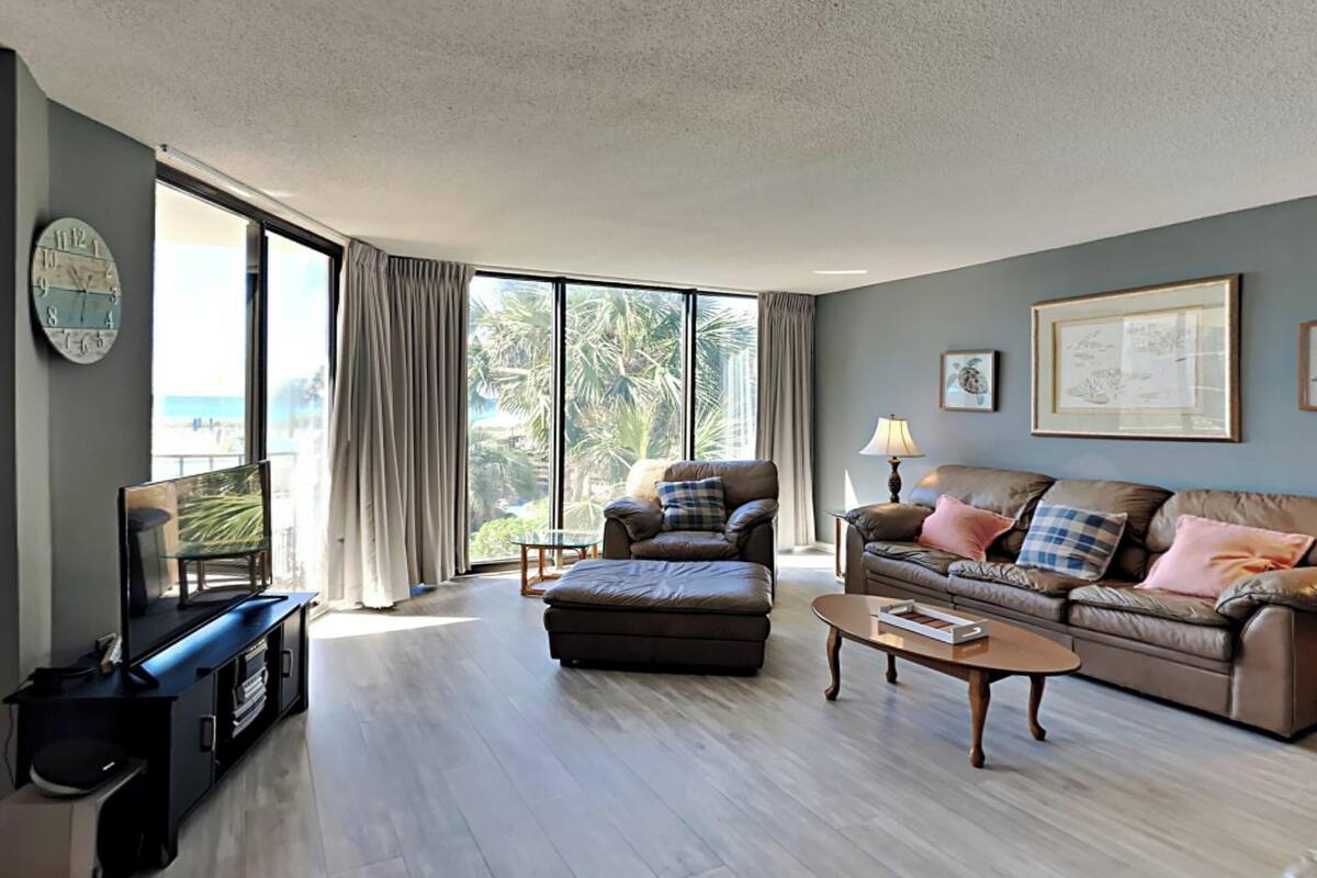 A spacious living room with a large window, a sofa, a coffee table, and a television on a stand.