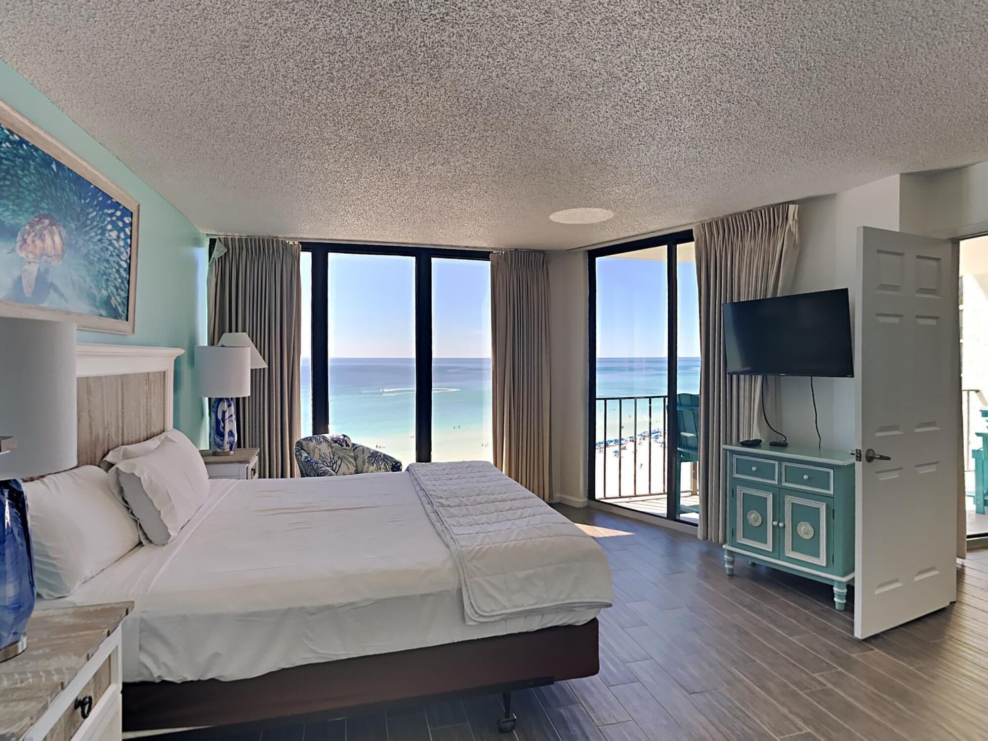 A spacious hotel room with a large bed, a television, and a view of the beach.